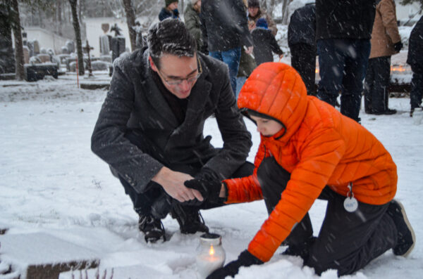 A man and a young boy kneeling in the snow and lighting a candle.