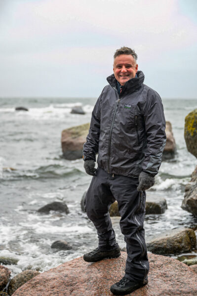 A man standing on a cliff with the stormy sea in the background.