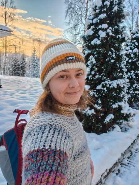 A woman in a knit sweater and knit hat is standing in a snowy landscape.