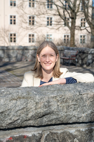 A smiling woman leaning an arm on a stone wall.