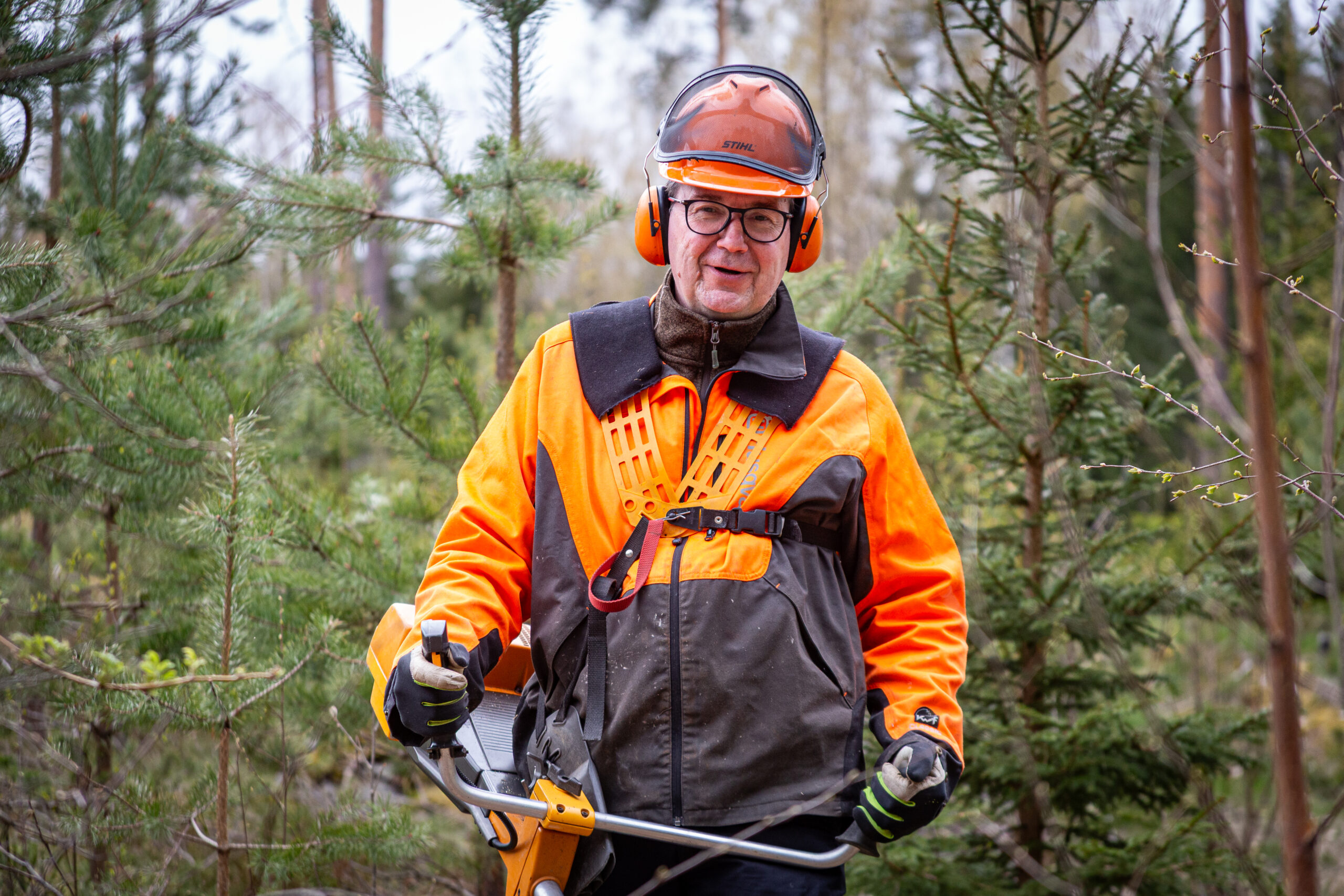 A man in orange safety gear in the forest.