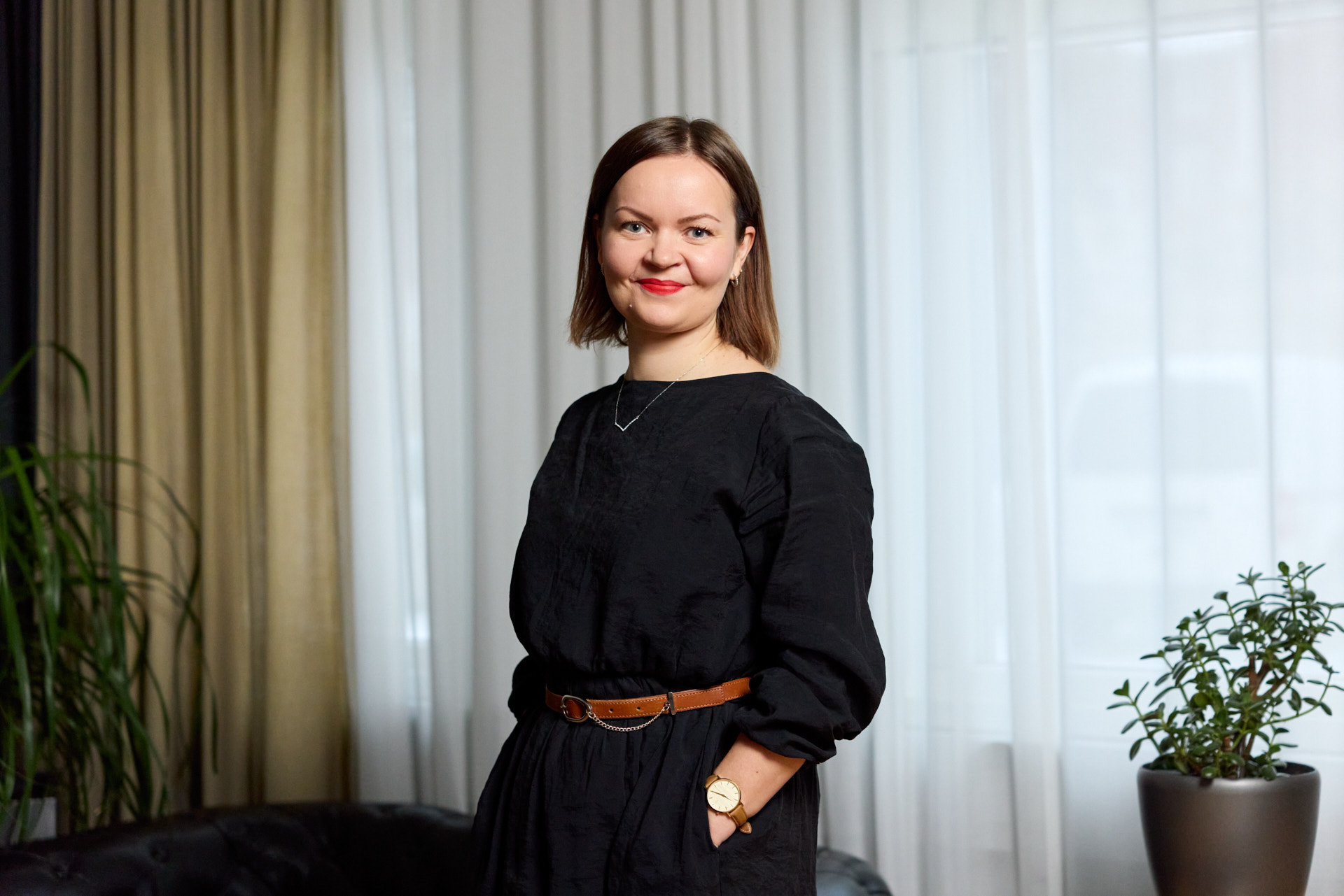A woman in a black dress posing in front of a draped window.