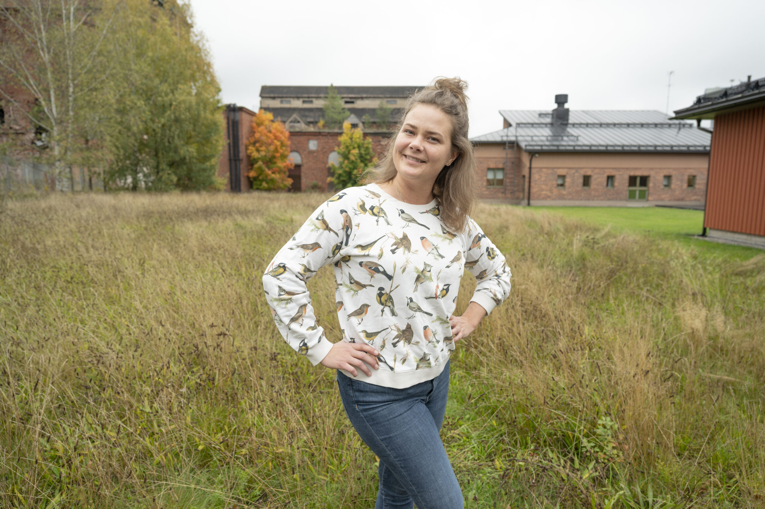 A woman with her hands on her hips is posing outside in a field.