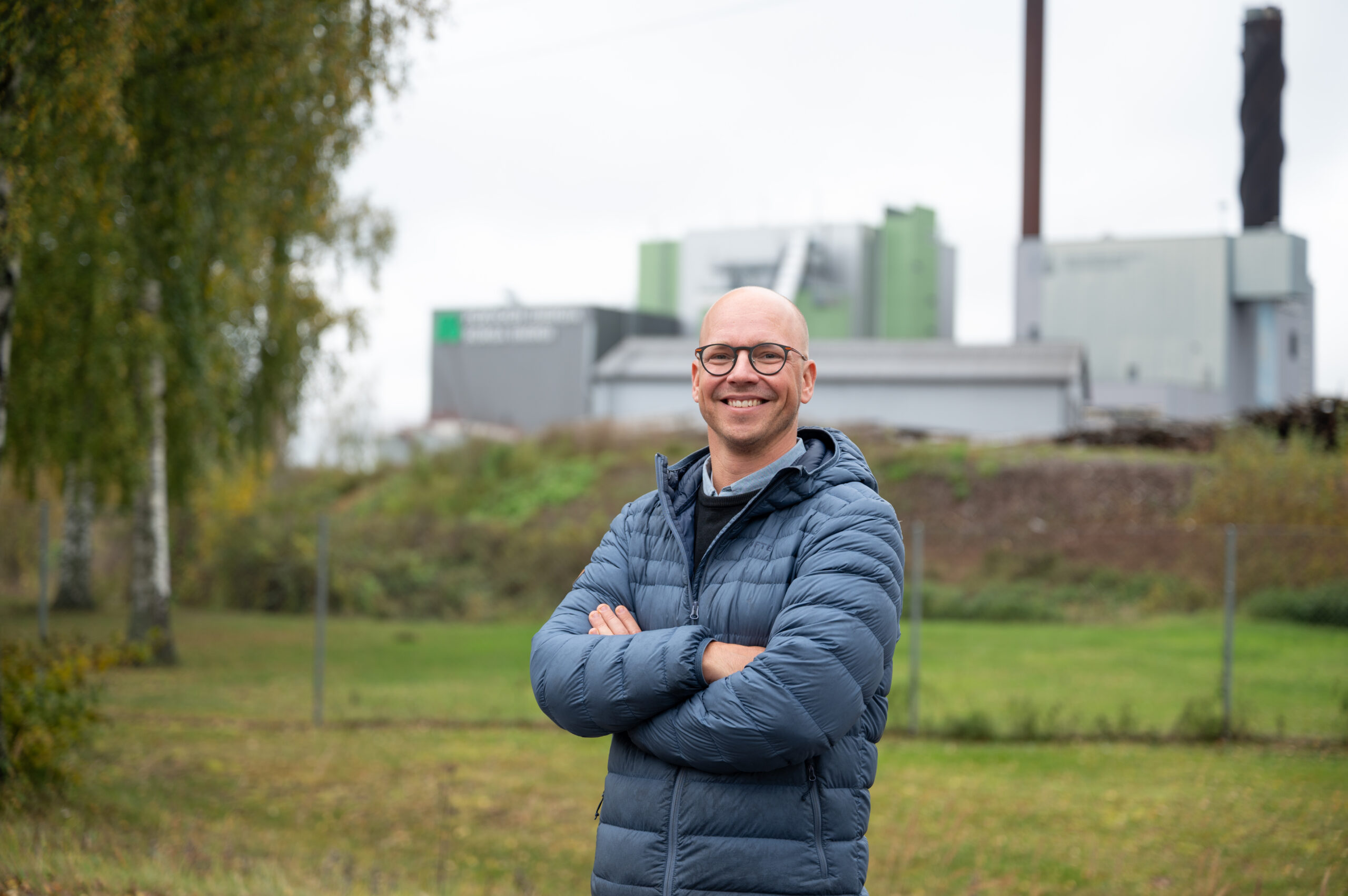A bald man with glasses standing with his arms crossed and smiling widely.