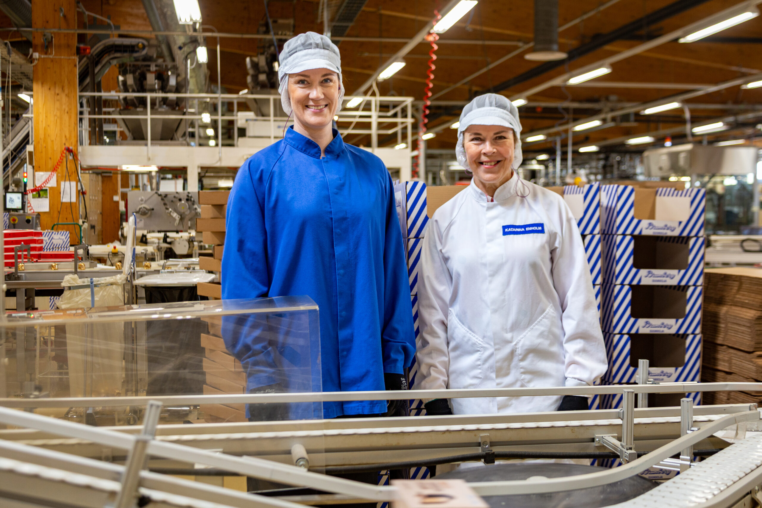 Two women posing behind a factory line.